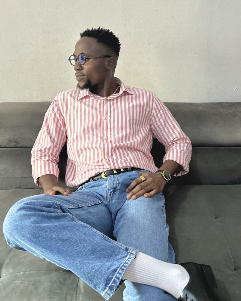Victor on a sofa in a pink and white striped shirt and blue jeans